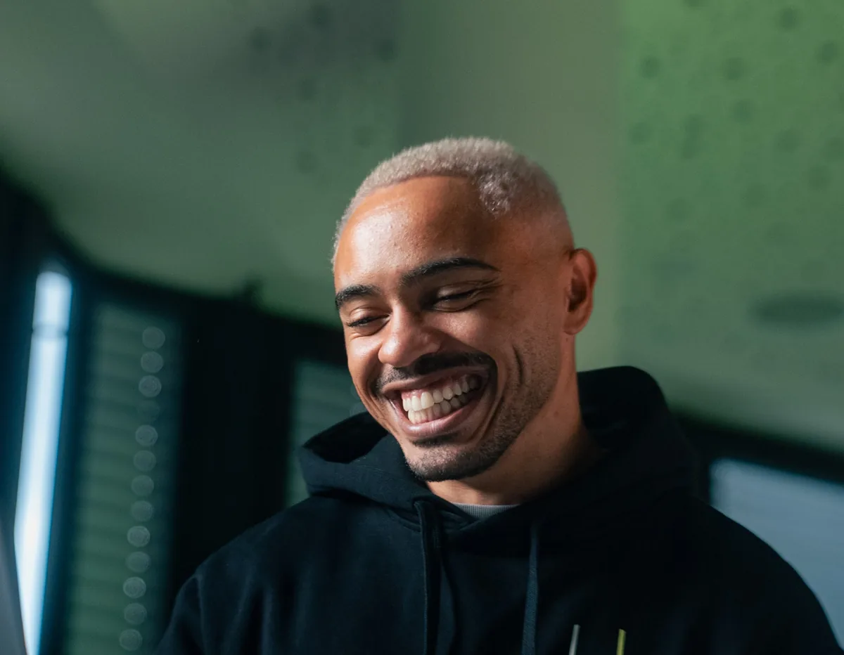 Marcos Da Costa lacht im COSTA-Hoodie vor dem Laptop